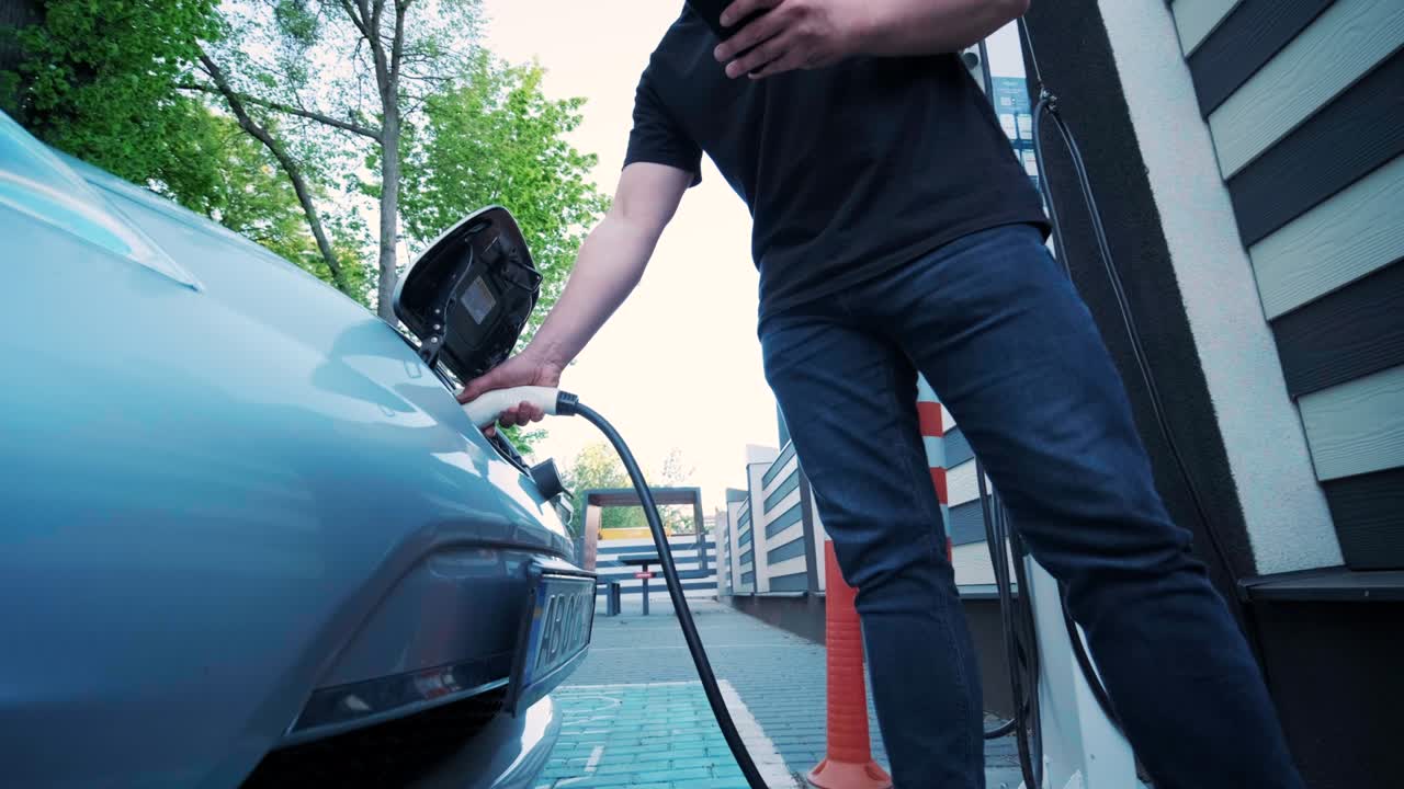 процесс заправки электромобиля. выстрел под люком, где заряжается электрический экомобиль. люк зарядки электрического автомобиля открывается автоматически. мужская рука вставляет эректильную машину