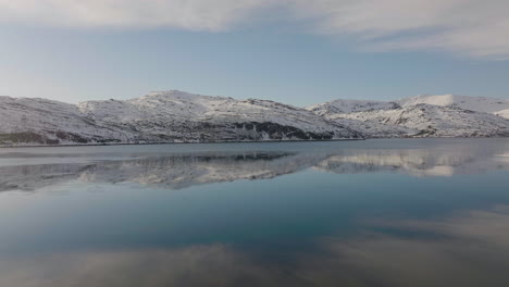 snowy mountains with blue sky reflections on beautiful calm lake in dafjord, ringvassoya, northern norway