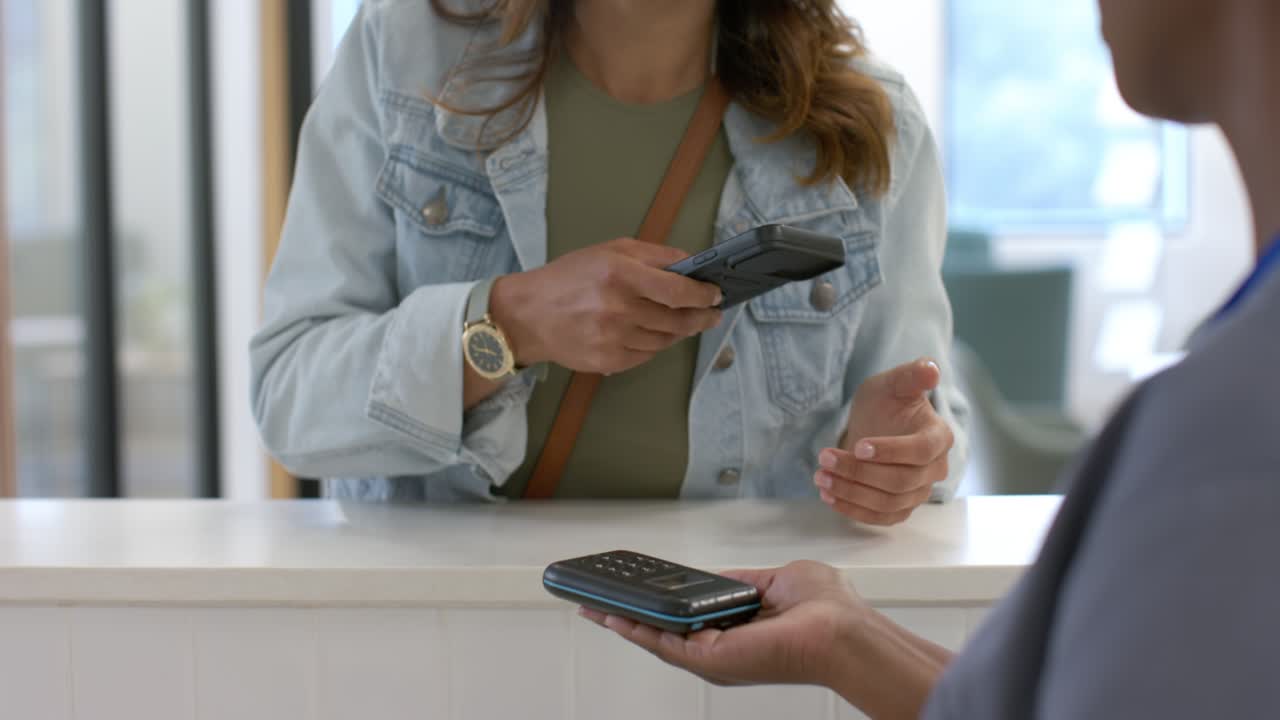 Una cliente di sesso femminile che utilizza il telefono per il pagamento contactless dopo che l'addetto alla reception le ha offerto il lettore