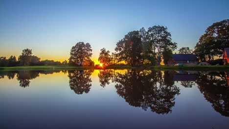 bright sun setting down behind lake and tree line near wooden rural cottage