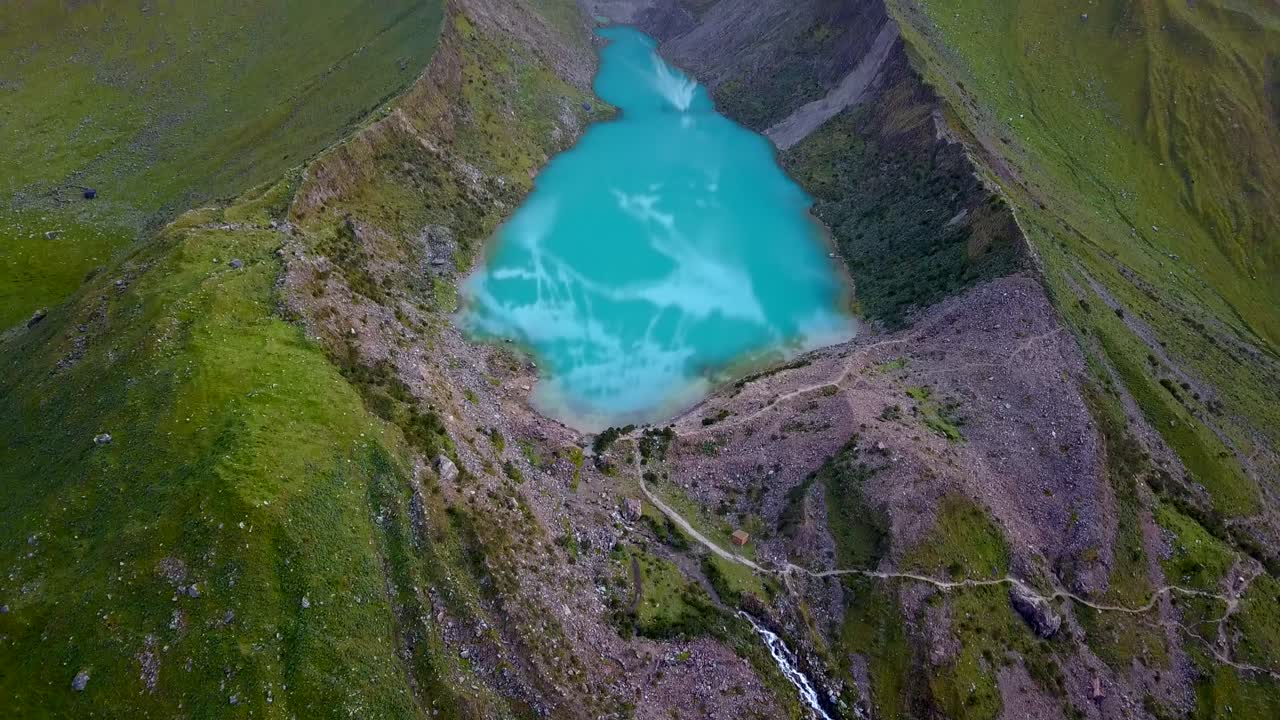 Aerial, reverse, drone shot tilting up revealing laguna Humantay lake, in Andes mountains, cloudy day, in Cusco region, Peru