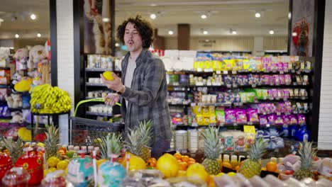 un chico moreno con el cabello rizado en una camisa a cuadros elige frutas en un supermercado mientras hace compras en una tienda de comestibles