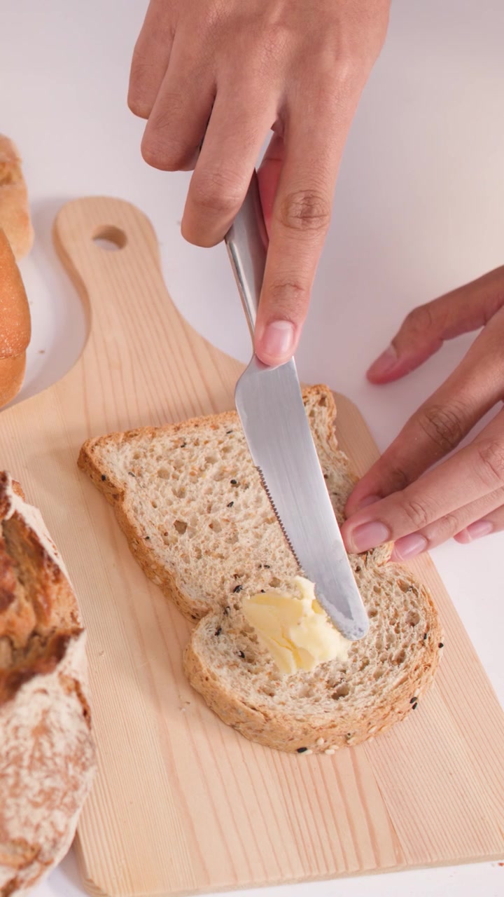 Person Spreading Butter on a Slice of Whole Grain Bread
