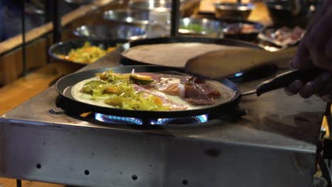 frying a pancake with bacon and vegetables in a street market in slow motion