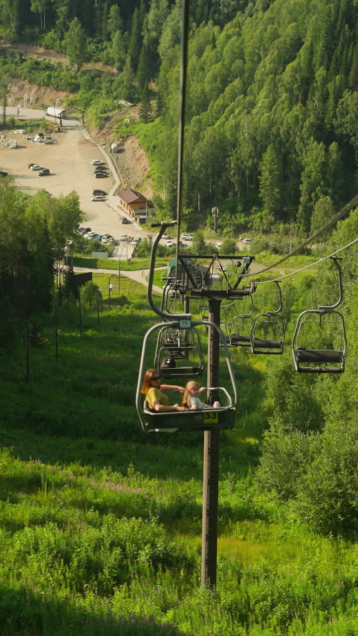 Tourists descend on funicular contemplating stunning view. Young people admire aerial view of astonishing resort with dense woodland and high mountains