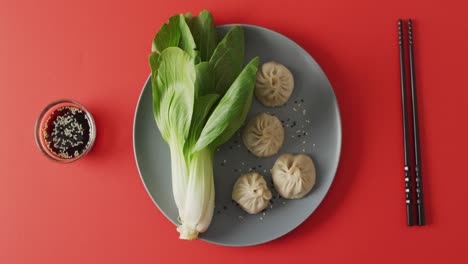 Composition-of-plate-with-dim-sum-dumplings,-pak-choi-and-chopsticks-on-red-background