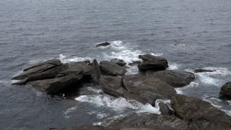 Static-shot-from-above-looking-over-to-large-rocks-built-up-on-coastline-with-crashing-waves-moving-over-them