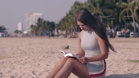 tremendous girl in light dress reads book sitting on sand