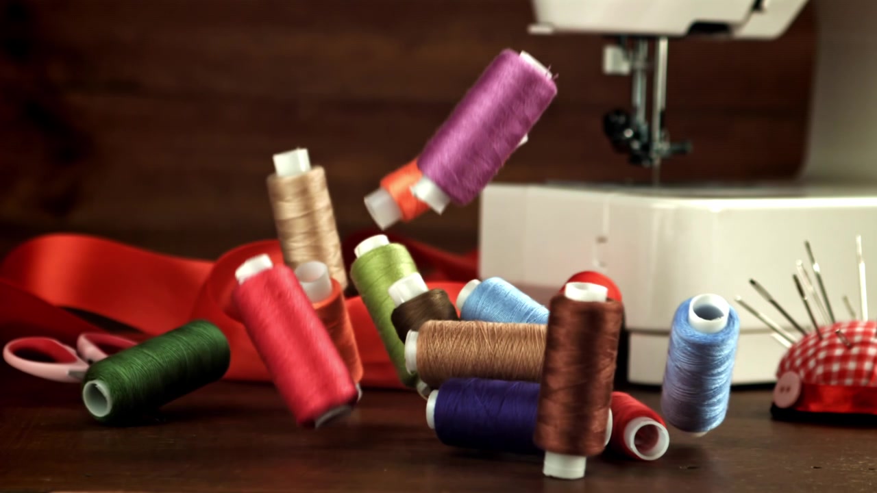 Colorful Spools of Thread Falling onto a Wooden Sewing Table