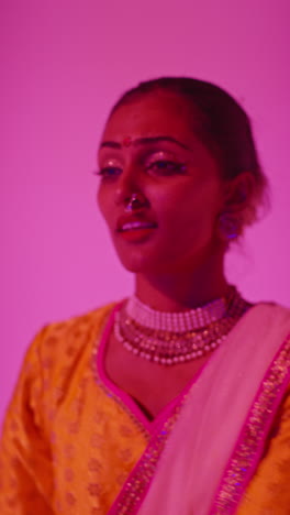 video vertical cabeza y hombros toma de estudio de una bailarina de kathak que realiza un baile vestida con un vestido tradicional indio contra un fondo púrpura