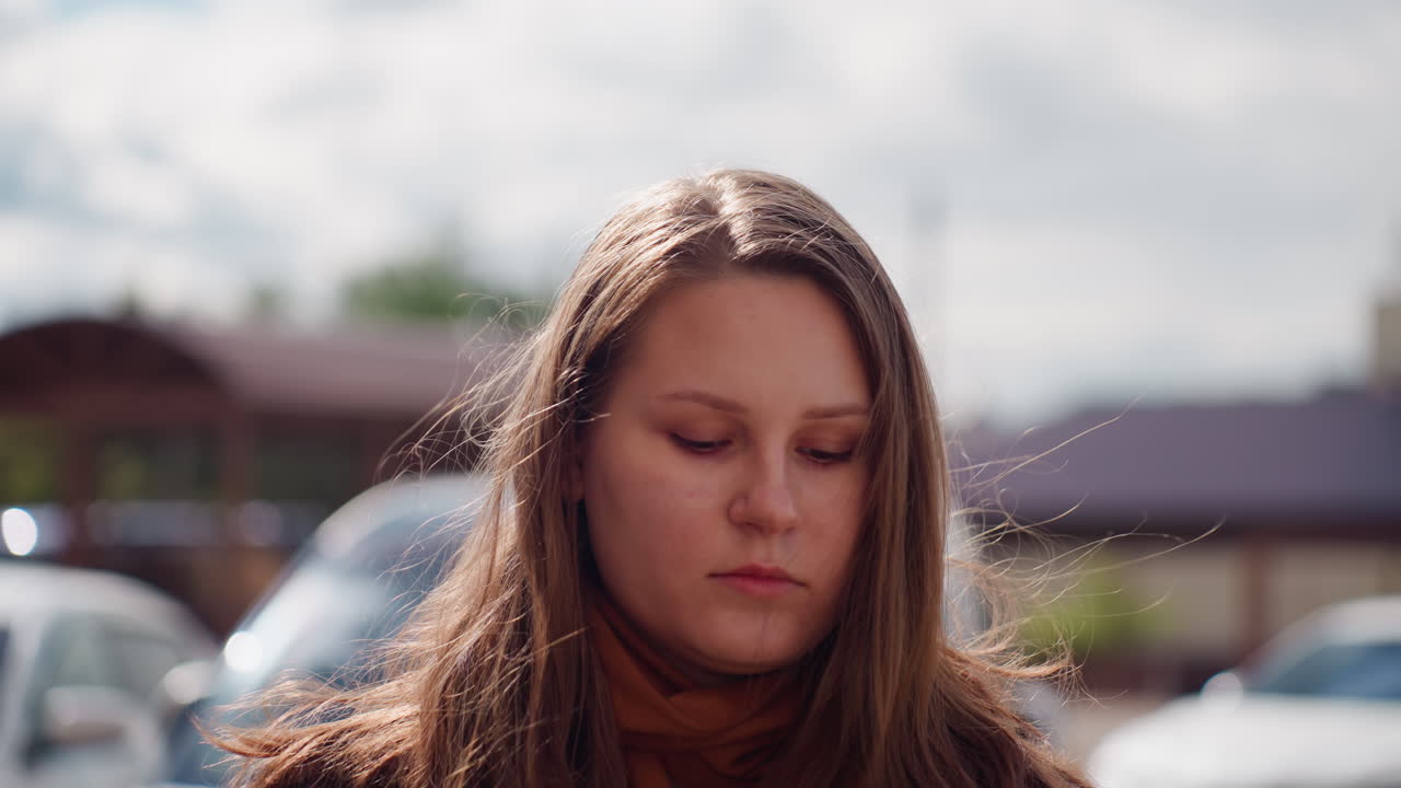 햇빛이 얼굴 윤곽을 비추는 동안 커리어우먼이 선글라스를 내리고 시선을 아래로 향하고 있어요. 도시의 고층 건물과 주차된 차들이 배경으로 흐릿하게 보이며, 밝은 오후에 조용한 야외의 순간이 집중력과 프로페셔널함을 전달하네요.