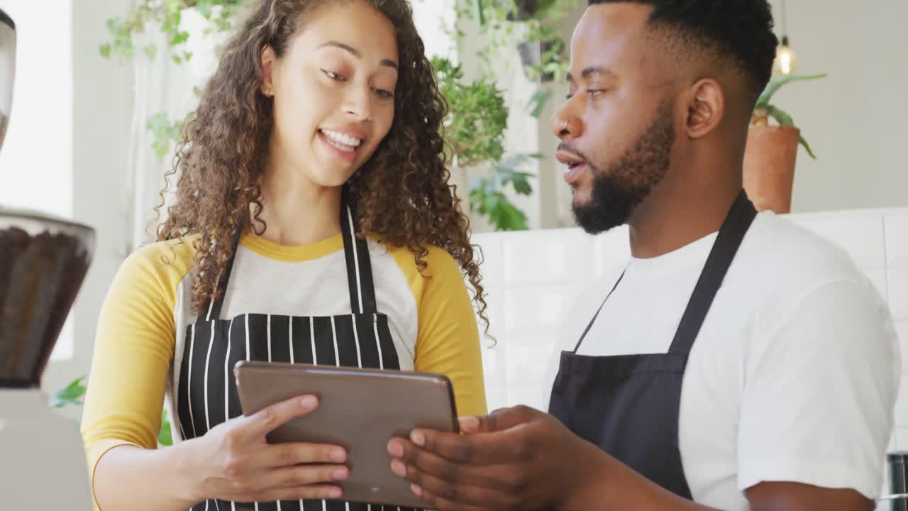 feliz dueño de un café afroamericano y barista biracial usando una tableta en el café