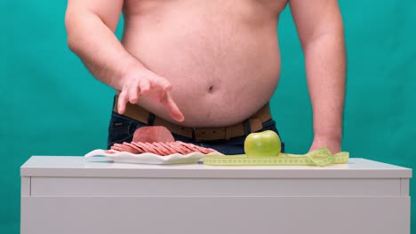 man with a fat belly chooses between sausage and a green apple. the concept of diet and willpower