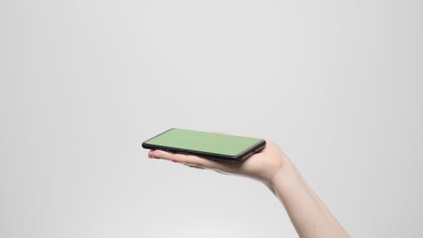 teléfono con una pantalla verde en la mano de una mujer sobre un fondo gris.