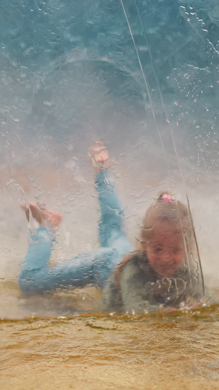 Joyful little girl jumps and falls inside large transparent water globe floating in small pool on gloomy spring day closeup slow motion
