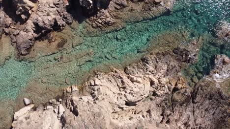 drone soars over a rock in the middle of the sandy beach of chia in sardinia's south, stunning weather