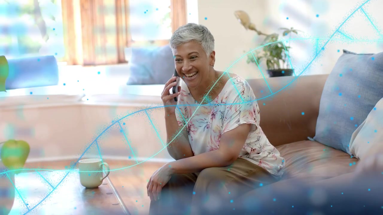 Donna che risponde al telefono, chinandosi, ridendo sul divano, con una sovrapposizione di DNA blu in movimento che mostra dati sulla salute.