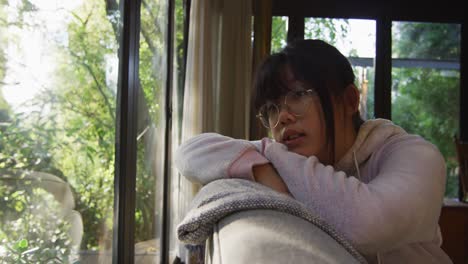 Asiatisches-Mädchen,-Das-Durch-Das-Fenster-Schaut-Und-Auf-Der-Couch-Liegt