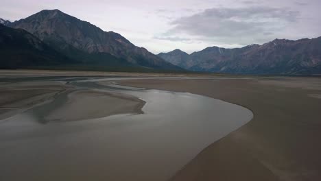 悠康湖 (yukon kluane lake) 上空的宏伟逆向飞行, 闪闪发光的水与沙<unk>的泥<unk>入口, 背景是崎岖不平的山脉, 在云天天, 加拿大, 上空的空中撤退