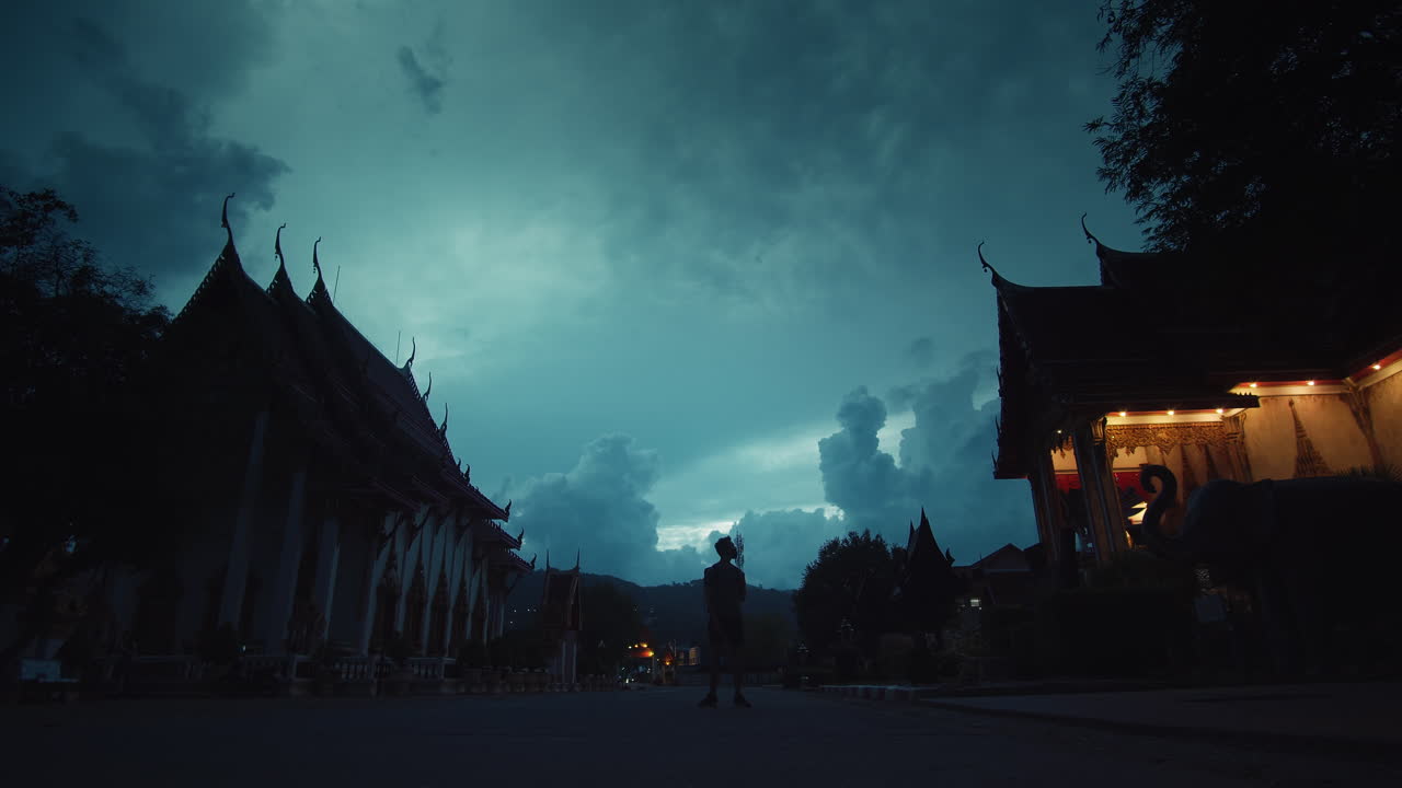Silhouette of Person Walking Through a Thai Temple at Night