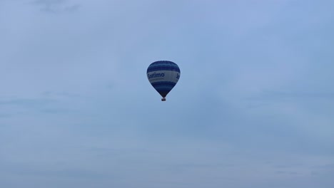 a blue hot air balloon floating skyward in a cloudy sky