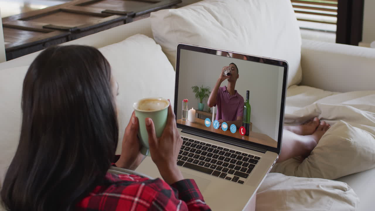African american woman holding a coffee cup having a video call on laptop sitting on couch at home