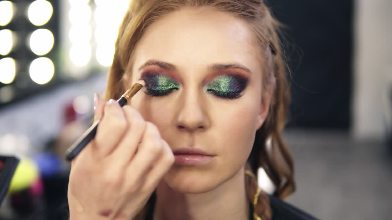 el maestro del rostro hace los últimos toques para los ojos maquillaje para una hermosa modelo con ojos de camaleón maquillaje efecto . vista frontal
