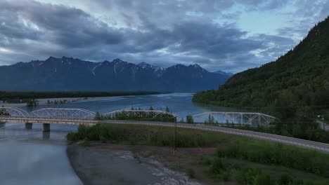 old railway bridge over knik river with mountain backdrop on a cloudy day in palmer, alaska