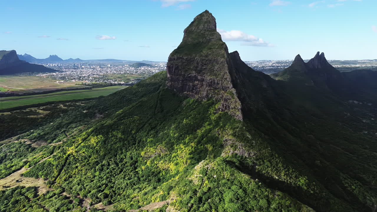 Veduta aerea con drone di una drammatica cima montuosa vulcanica circondata da verdi colline con il paesaggio urbano visibile in lontananza a Mauritius