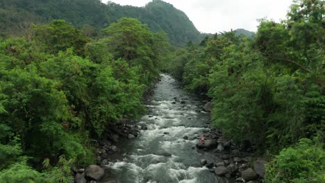 tropical lush jungle with wild river and girl meditating in lotus pose on rock