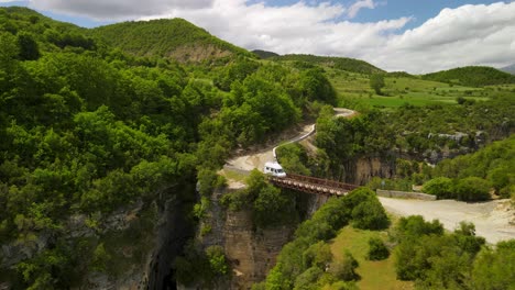 aerial perspective of a sunny day as a travel caravan crosses a bridge over osumi canyon in albania