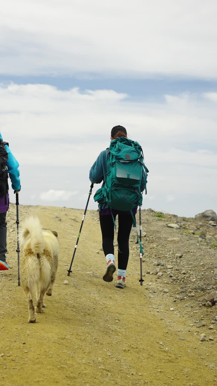 Due escursionisti e un cane che camminano su un sentiero di montagna