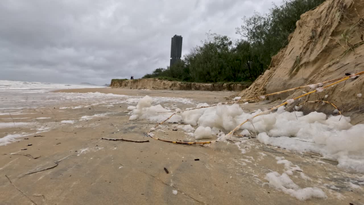 una escena de playa tormentosa con espuma y erosión, destacando el impacto ambiental y las condiciones climáticas turbulentas