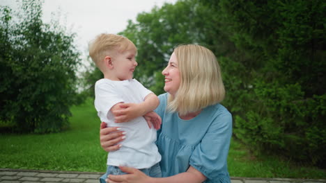a heartwarming moment of a mother and her young son sharing a joyful conversation outdoors, with a lush green background