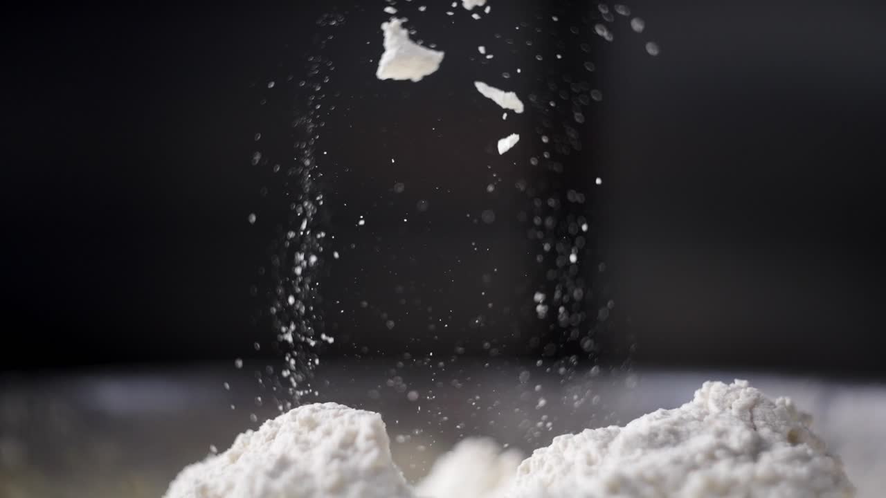 Beautiful cinematic and slow motion view of a hand mixing dough and flour in a fancy kitchen, flour falling and flying in the air. Particles and specks of flour suspended in the air.