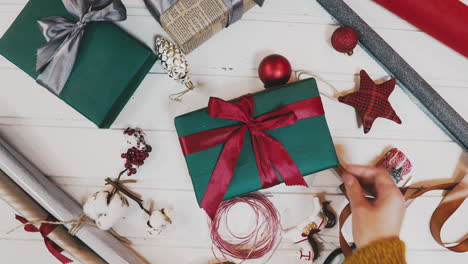 christmas gift giving - someones hand in red knitted sweater making bow on red box with present, banner with copy space