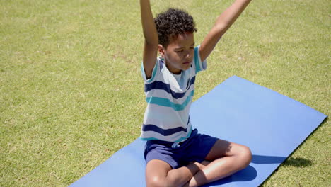 biracial boy practicing yoga outdoors on a blue mat