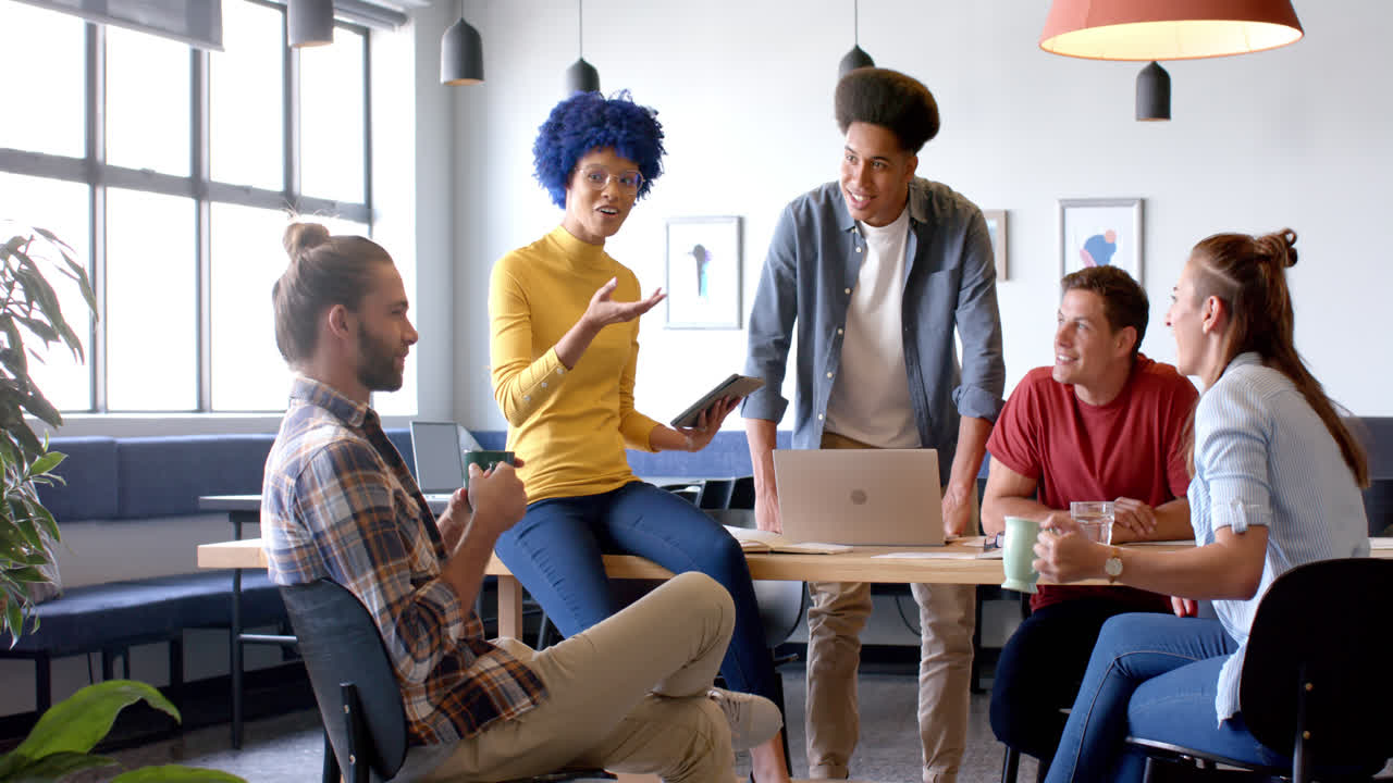 Happy diverse business creatives using laptop in discussion in casual office meeting, slow motion