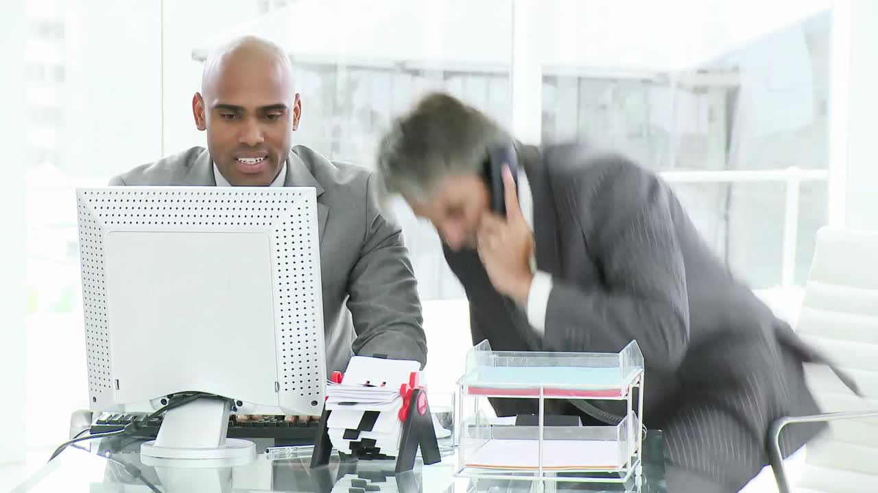 Two angry businessman on phone working at a computer