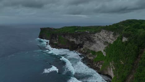 dark clouds gather above the uluwatu cliffs as big waves crash against the rocks