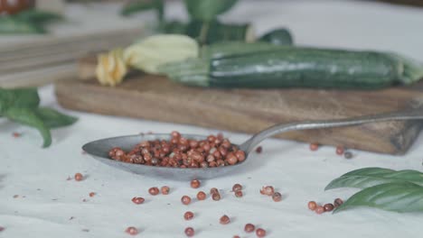 A-silver-spoon-full-of-red-pepper-bounces-against-the-table-and-peppercorns-fall-all-around,-there-are-also-courgettes-and-basil-leaves-in-the-scene