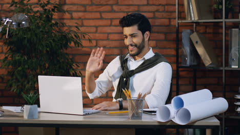 alegre hombre de negocios árabe que tiene un videochat en la laptop mientras está sentado en la acogedora oficina en el escritorio