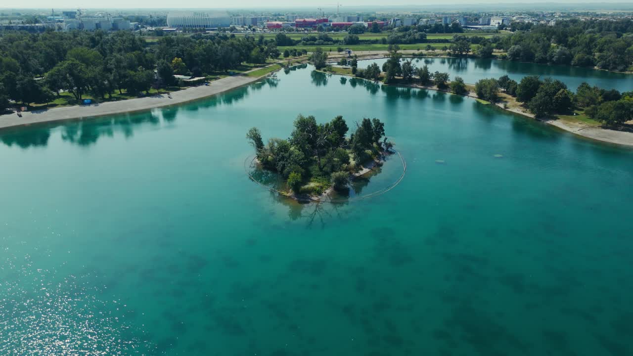 aerial - small tree covered island surrounded by clear turquoise water and sandy lake shores