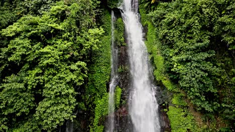 Drone-shot,-The-image-captures-a-verdant-waterfall-surrounded-by-lush-green-foliage,-taken-from-a-high-vantage-point-that