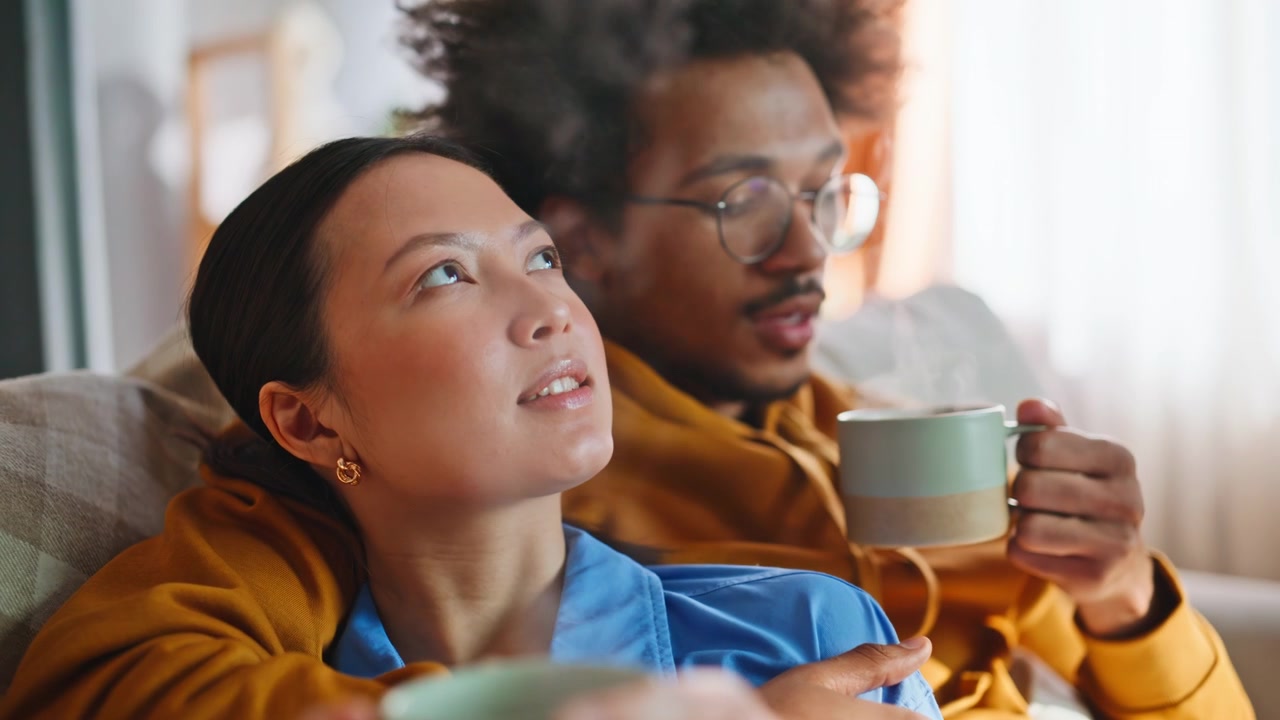 Closeup couple relaxing on sofa with steaming coffee mugs. Cozy home morning