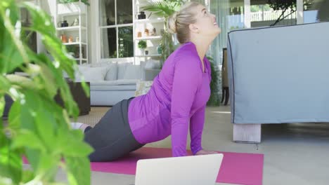 mujer caucásica feliz de talla grande practicando yoga y usando una computadora portátil en cámara lenta