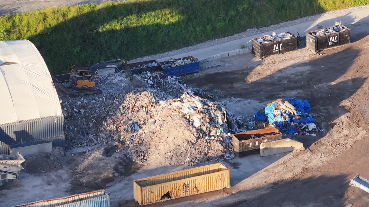 Ripresa con drone di macchinari pesanti che spostano rifiuti in un centro di riciclaggio in pieno giorno.