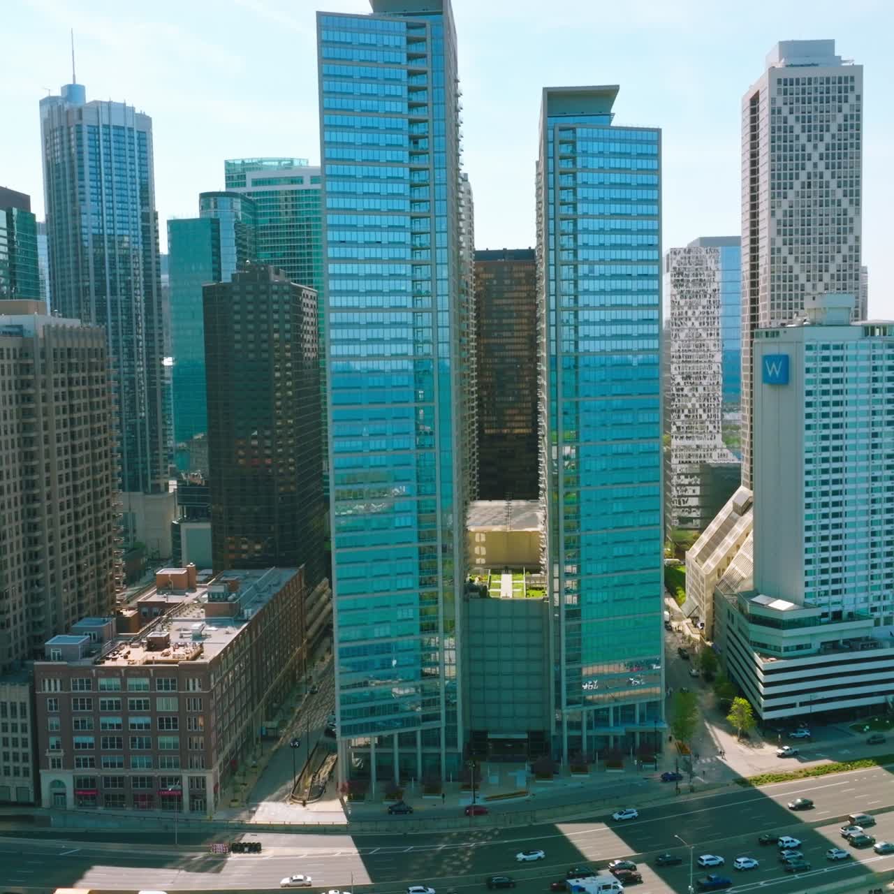 Blue skies and turquoise waters reflecting in the mirror windows of skyscrapers. Multi-line road with busy traffic near the buildings