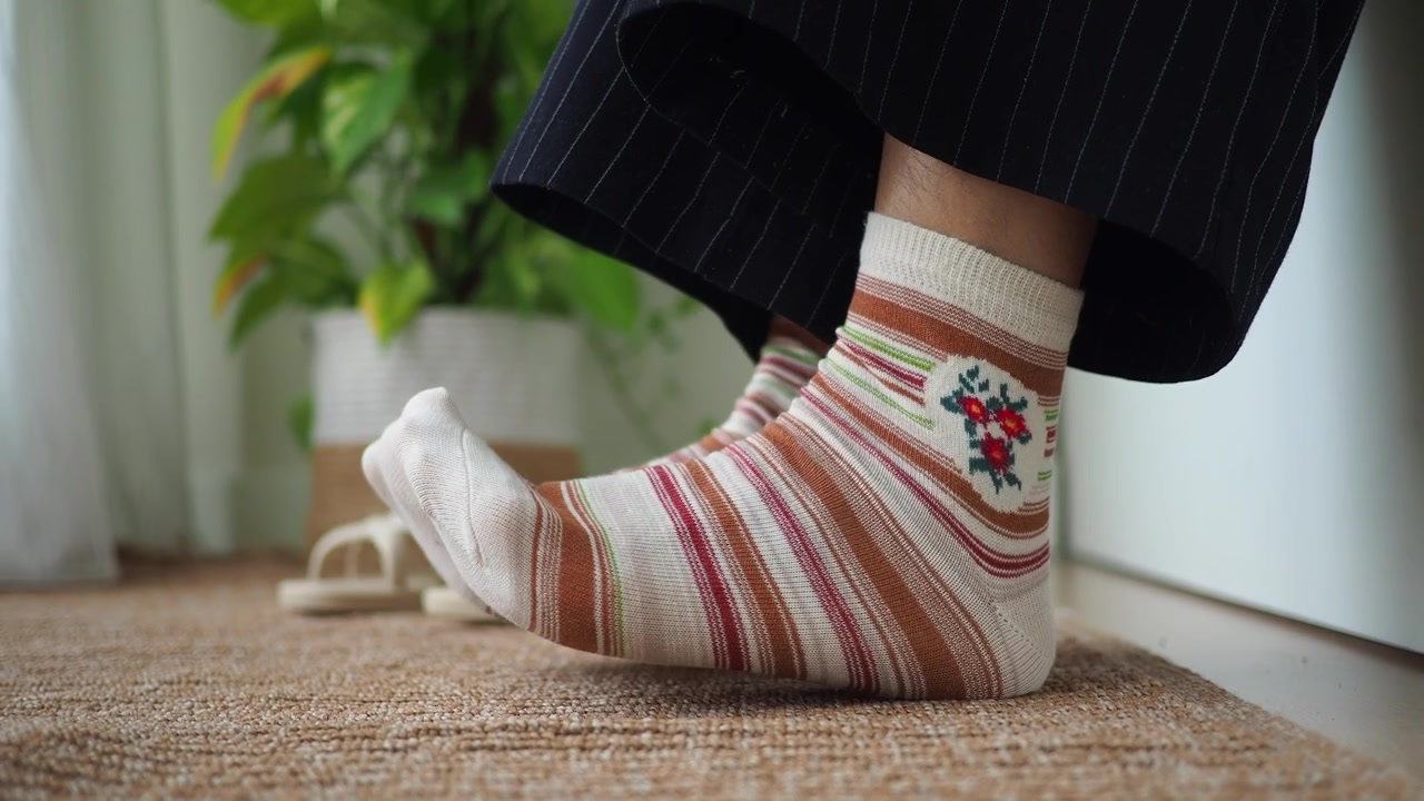 Persona con calcetines a rayas y bordado floral sentada en el interior