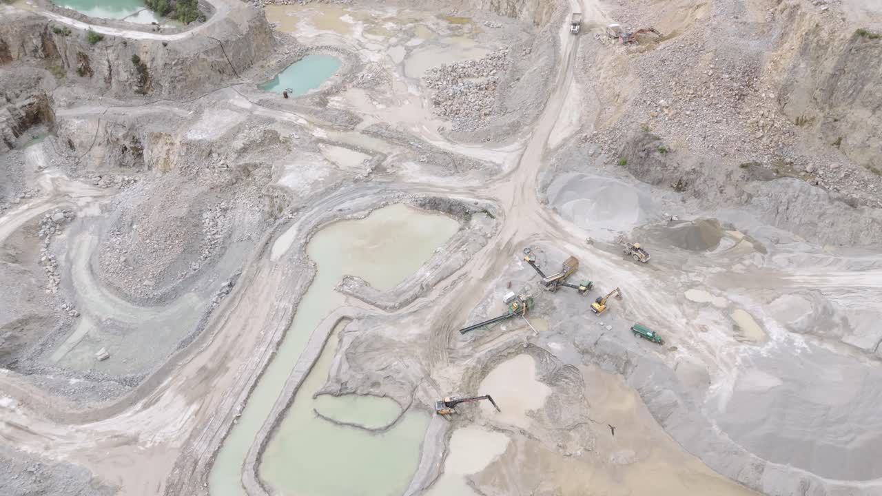 Orbital drone shot capturing the earth-moving team working at the bottom of an aggregate quarry with machinery and activity